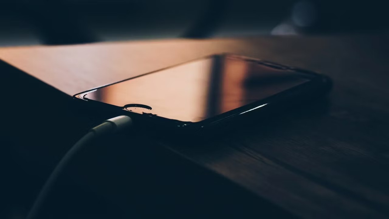 روش درست شارژ کردن آیفون 2 آیفون 7 روی میز قرار گرفته و با کابل شارژ سیمی شارژ می شود